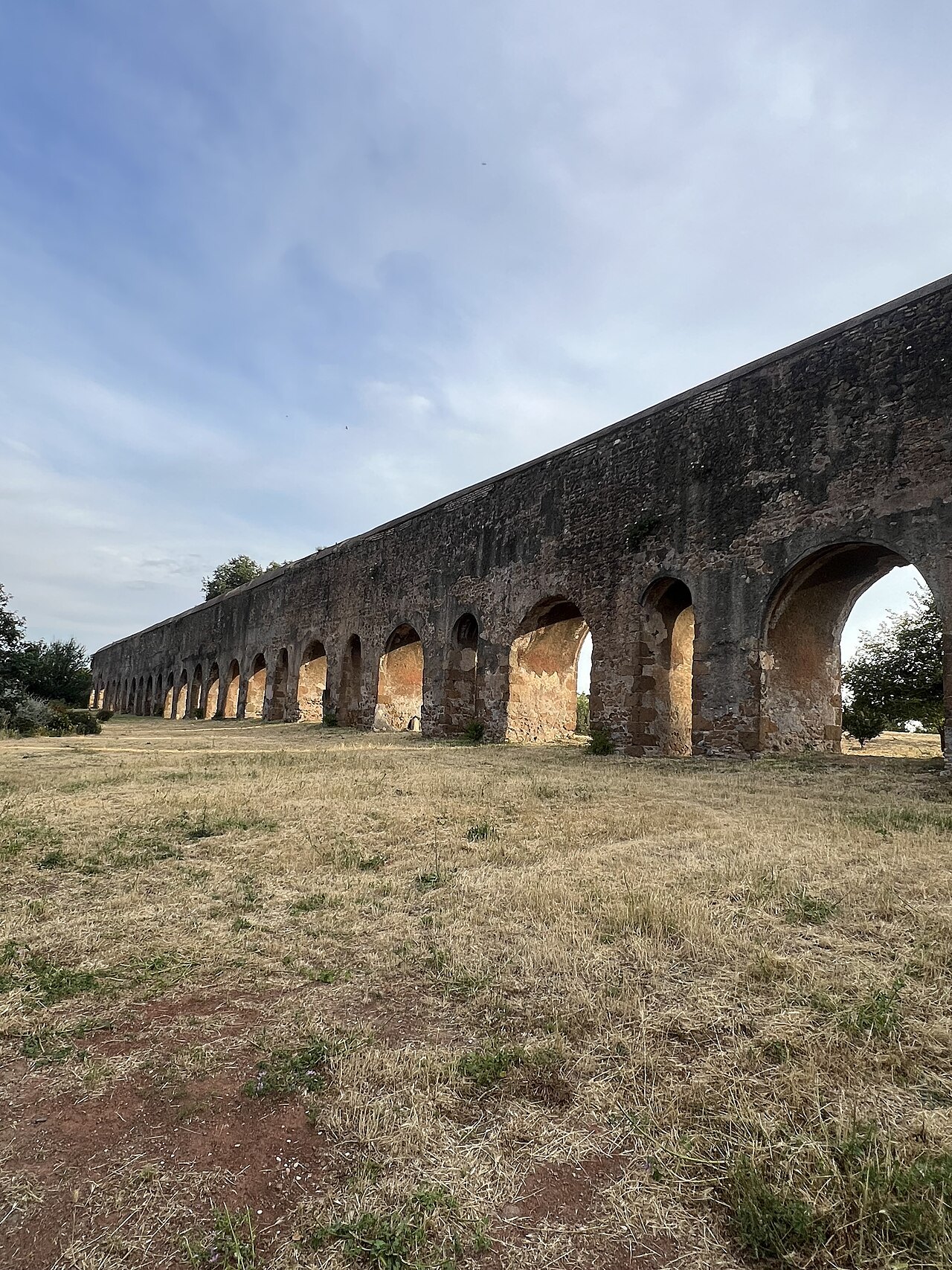 The arches of the Acqua Felice aqueduct running across a dry field
