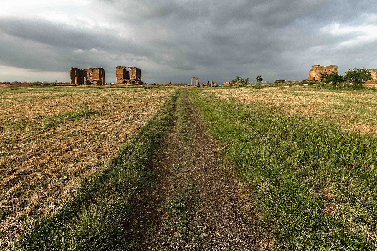 A track through golden grass toward the brick ruins of the Villa of the Quintilii