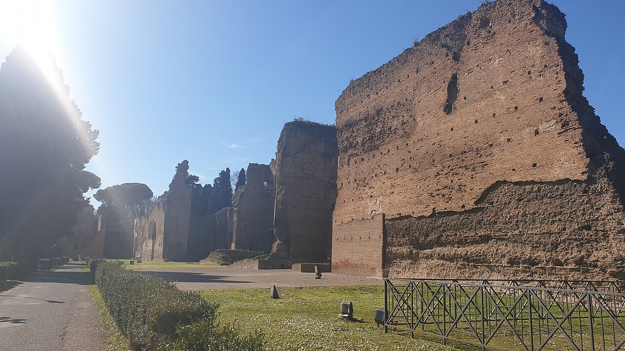 A long run of high brick walls at the Baths of Caracalla, a path and lawn beside them