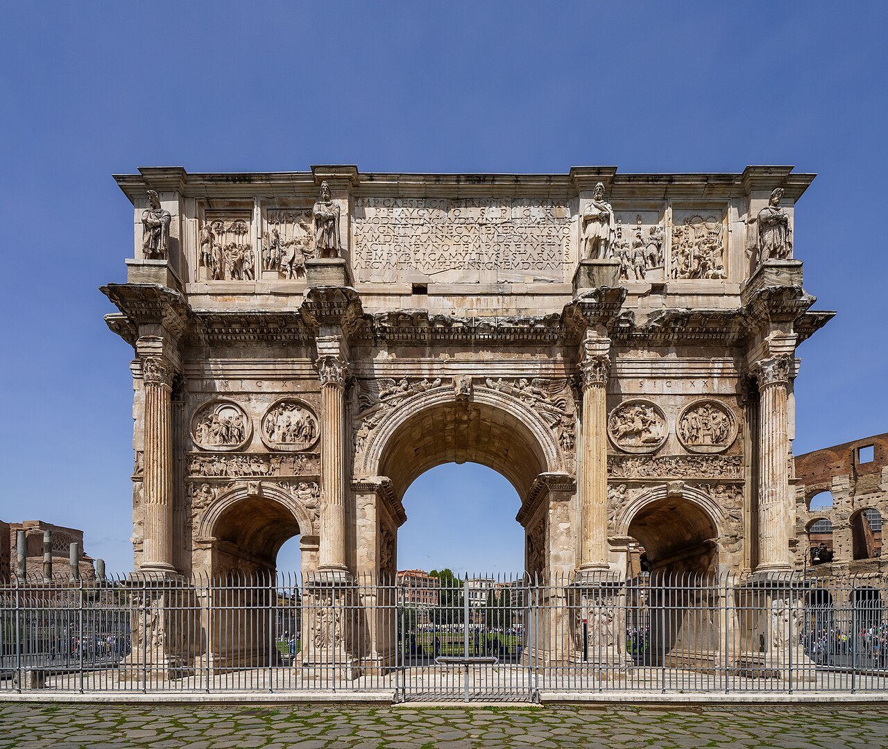 The Arch of Constantine against a blue sky, its three arches and carved attic