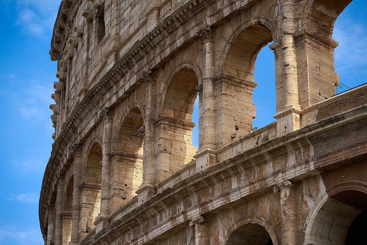 The curving arcades of the Colosseum from below, against a deep blue sky