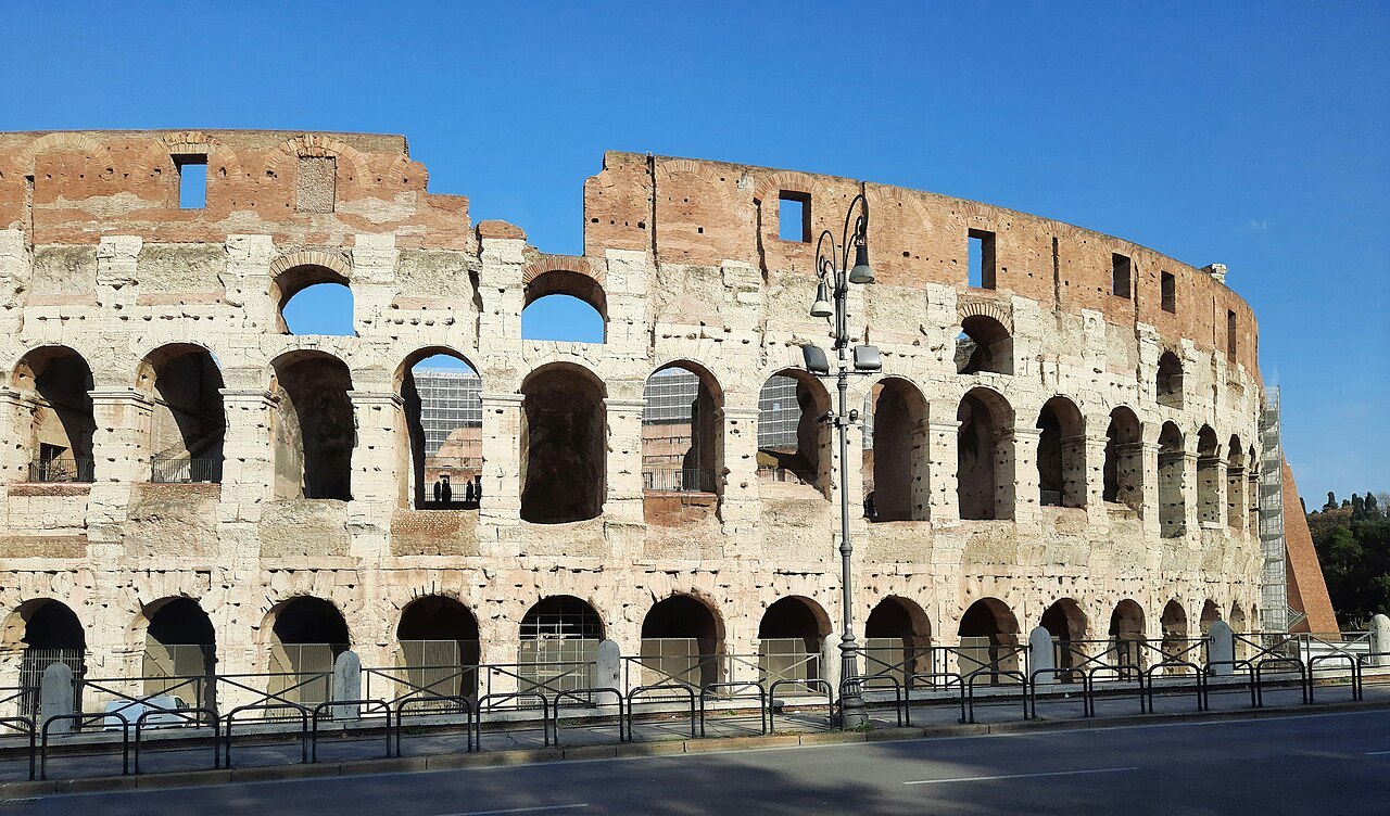 The outer wall of the Colosseum, its arches pale against a clear blue sky