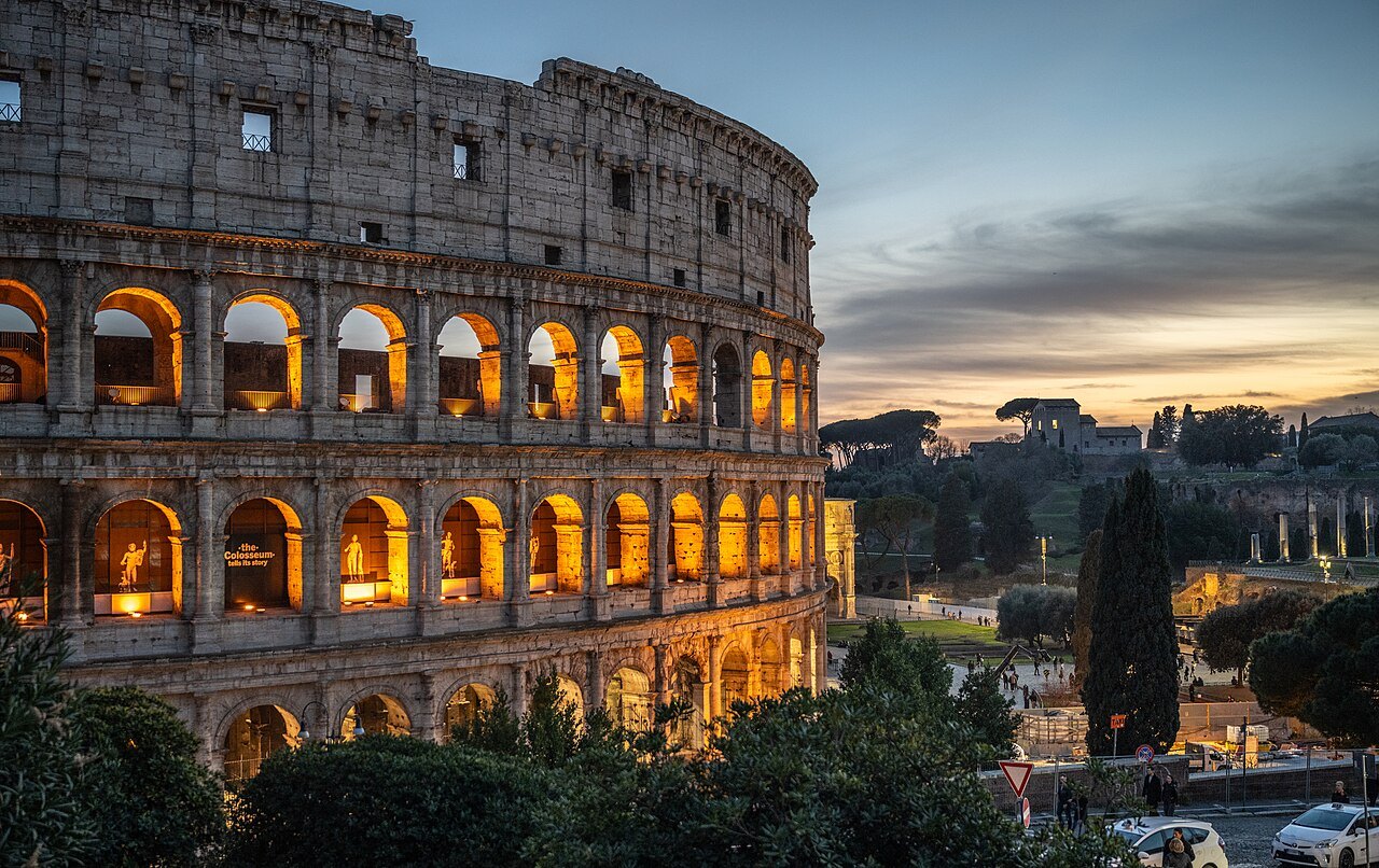 The Colosseum's arcades lit from inside at sunset, the Palatine's trees beyond