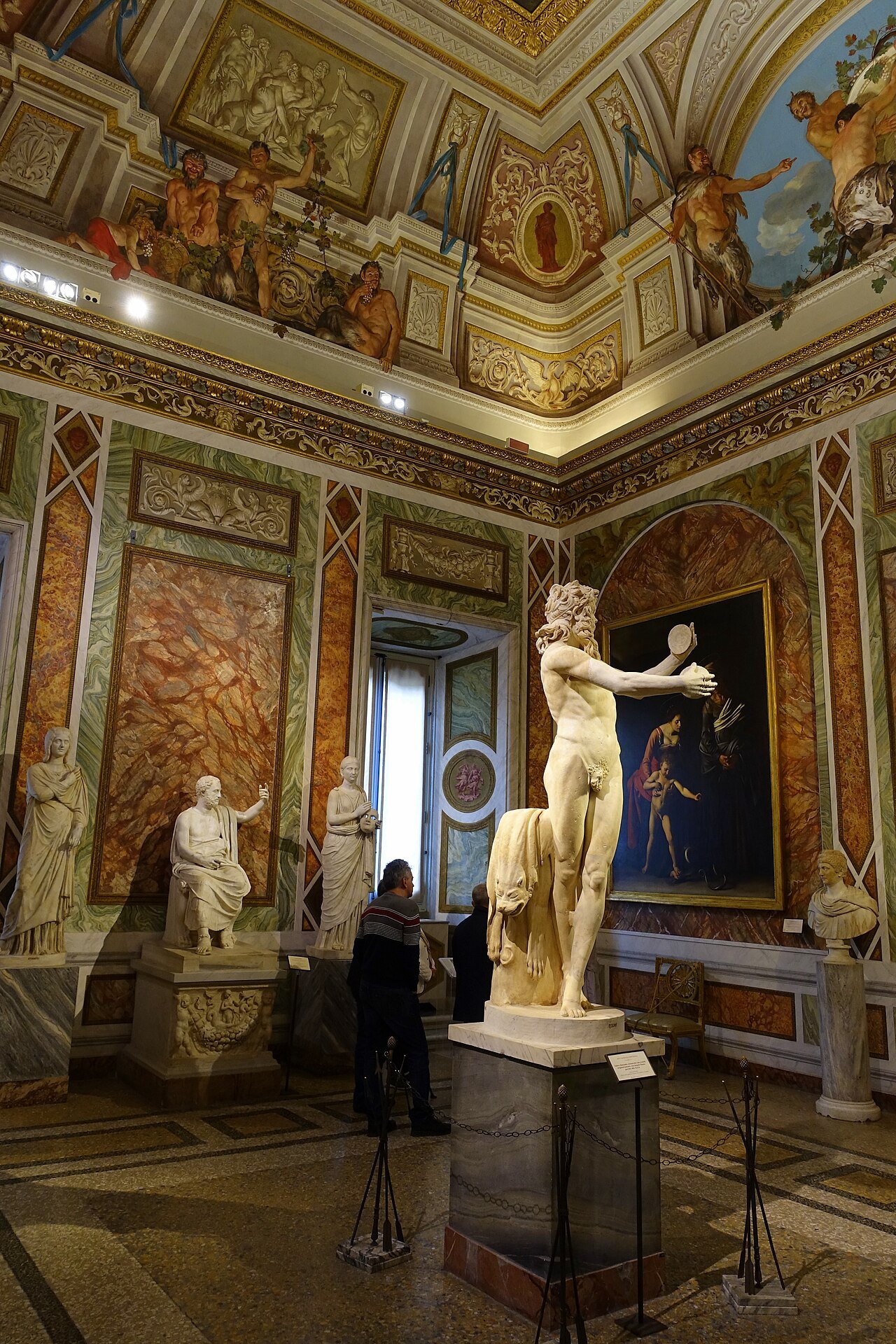 The Room of Silenus in the Borghese Gallery, a marble satyr in front of paintings on colored walls