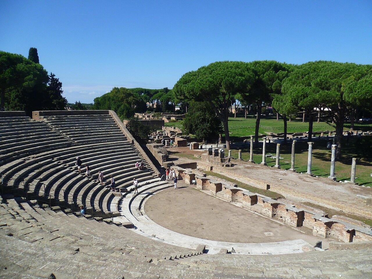 The theater of Ostia Antica, its curved stone seats facing the stage, pines beyond