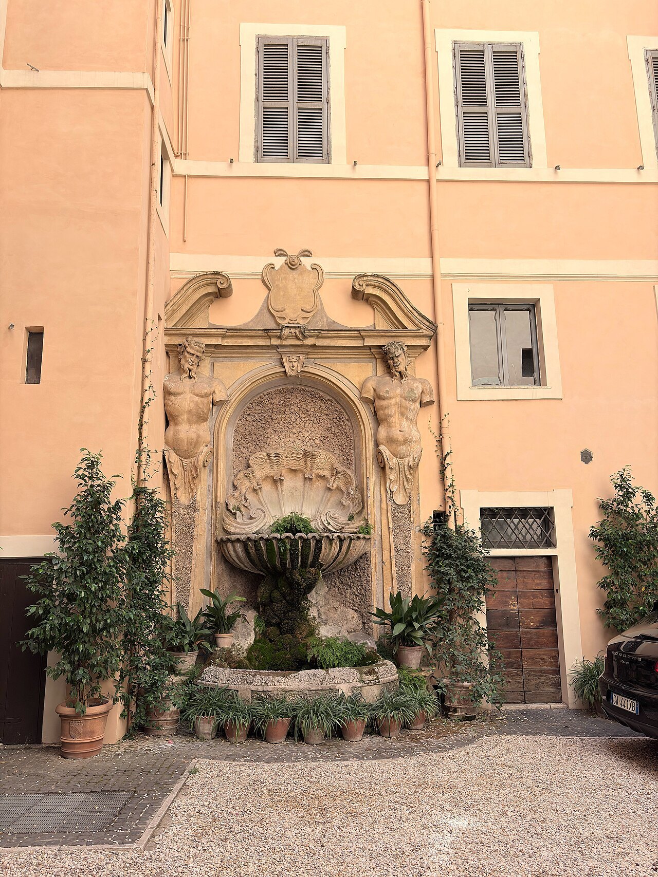 A wall fountain in a courtyard of Via Panisperna, framed by potted plants