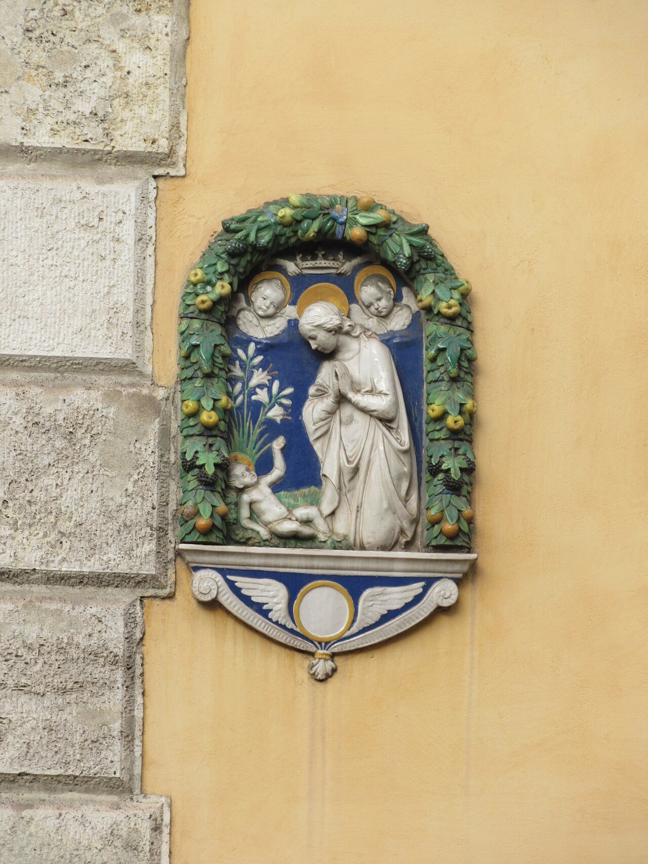 A glazed terracotta Madonna in a garland frame on an ocher wall in Parione