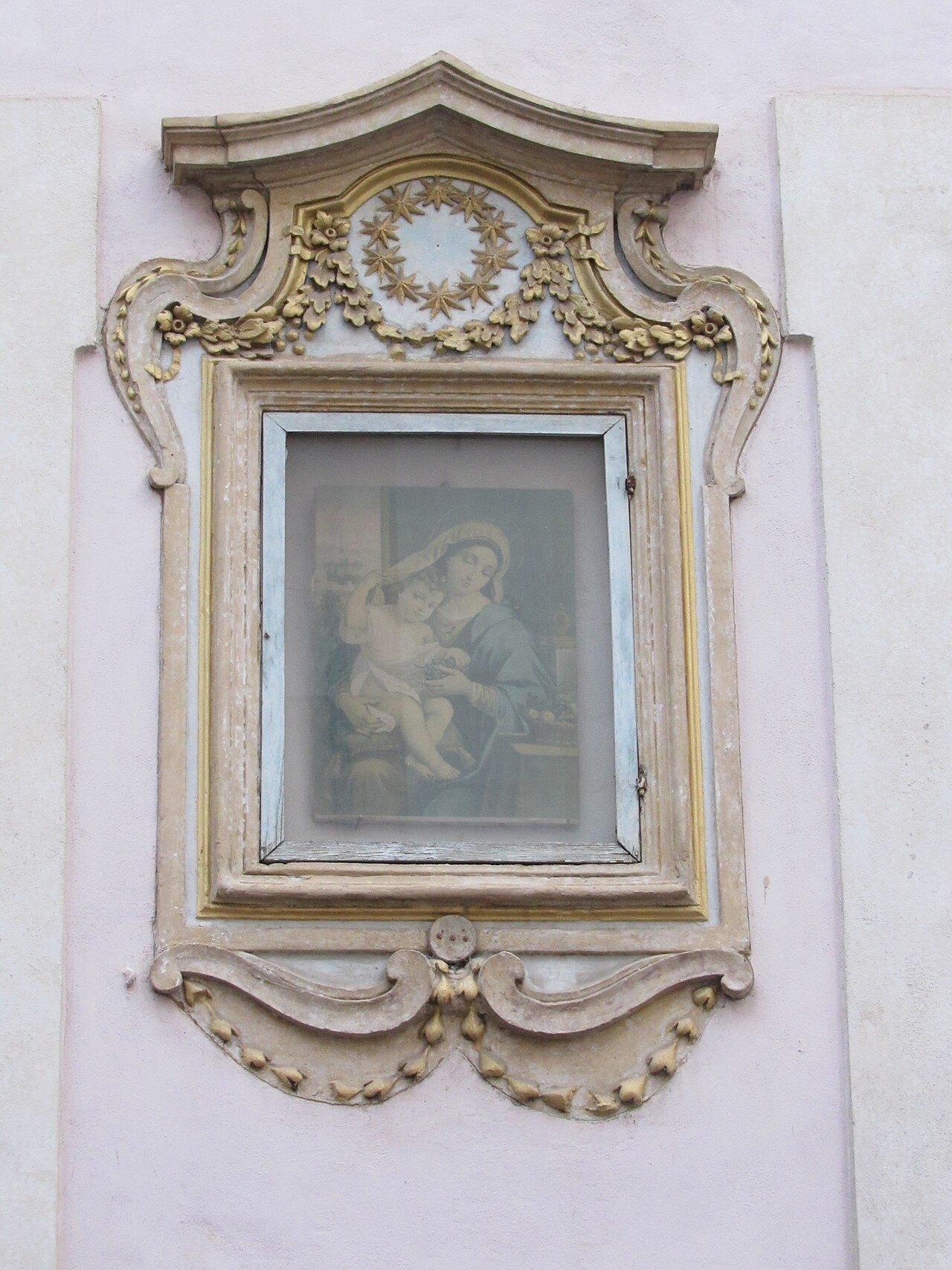 A small painted Madonna in a carved and gilded frame on a white wall in Sant'Eustachio