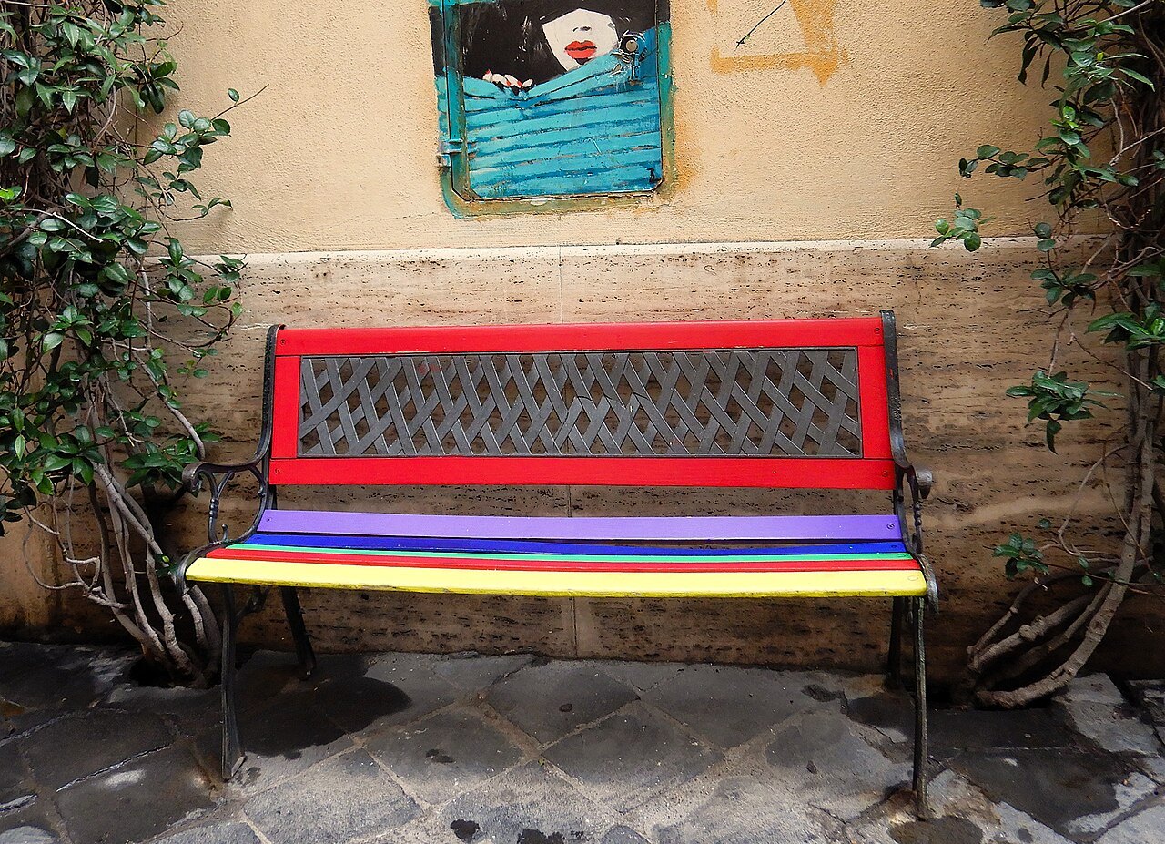 A bench painted in bright stripes against an ocher wall on Via Margutta