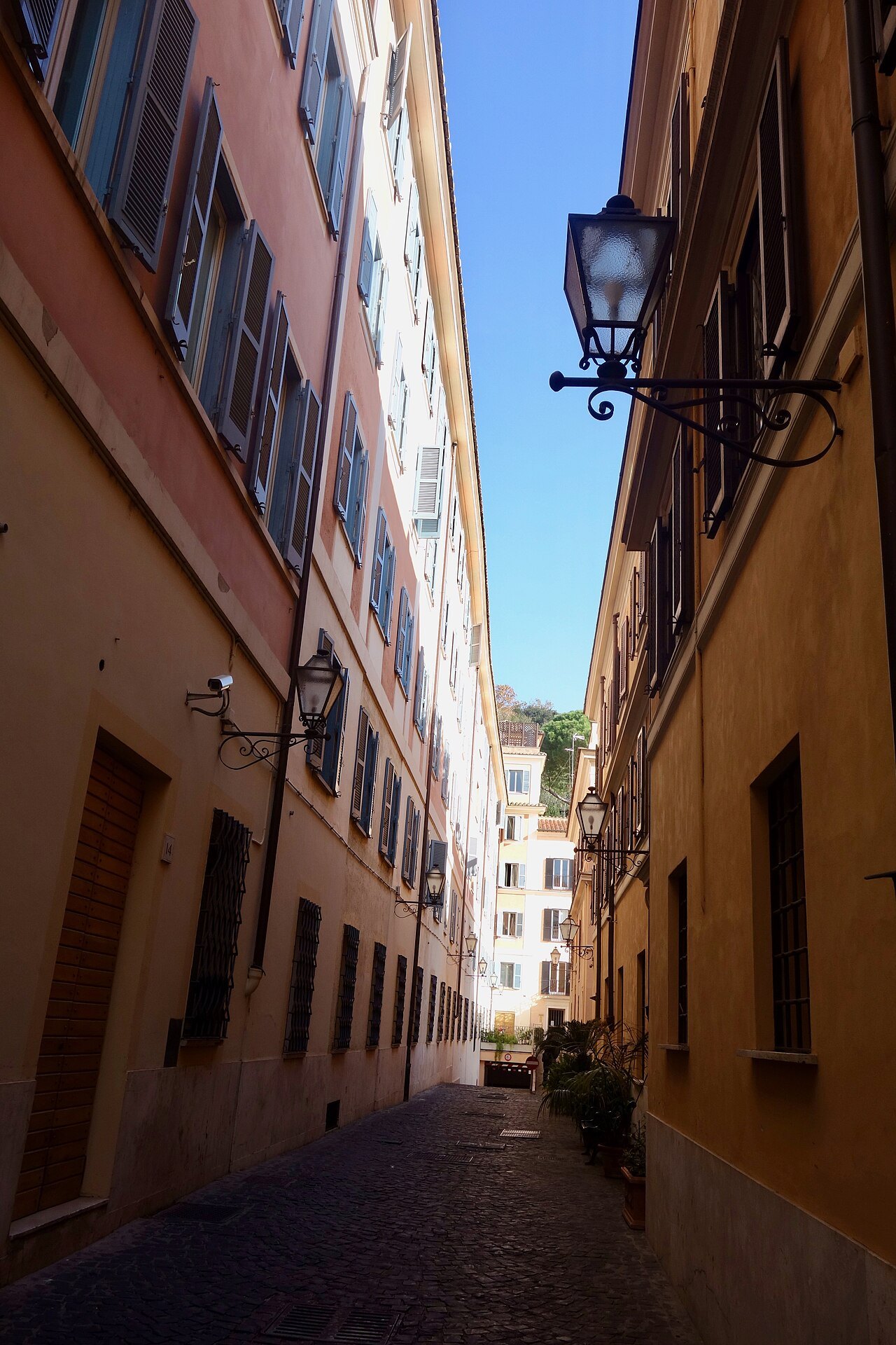 A narrow side alley off Via Margutta between tall ocher walls, a lantern on a bracket
