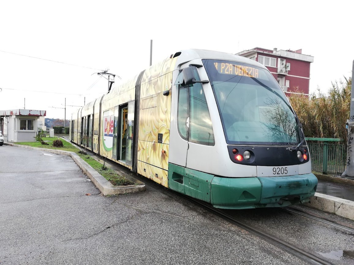 A modern green and white tram at a stop on the edge of the city