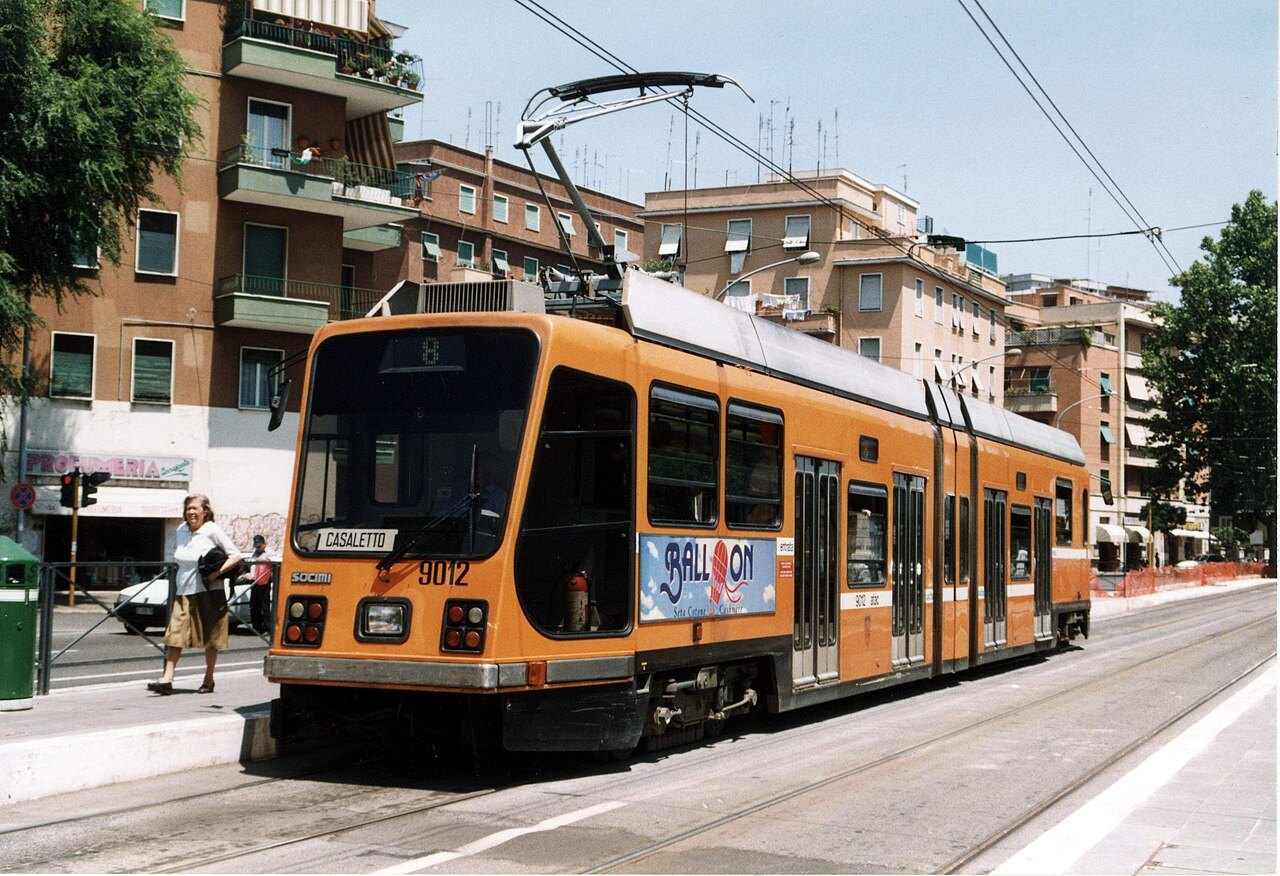 An orange articulated tram at a stop in a residential street