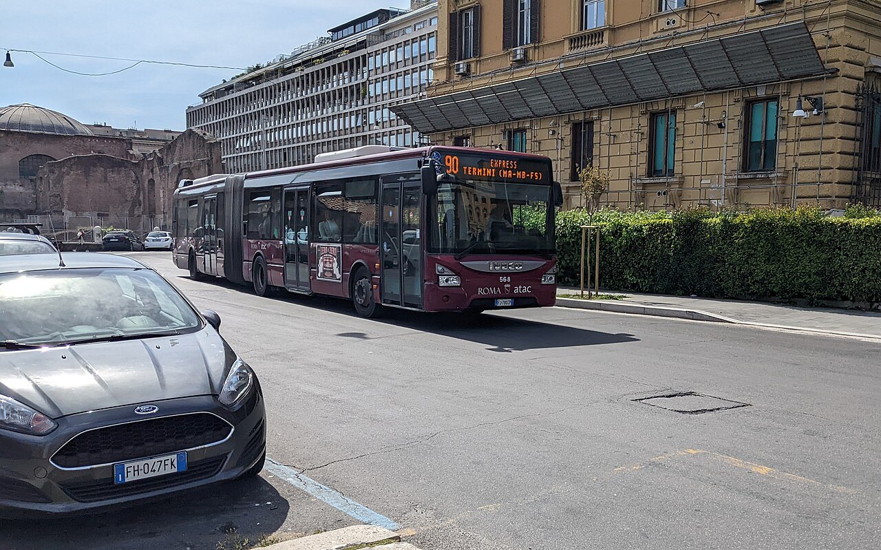A red articulated city bus on an express route, parked cars in the foreground
