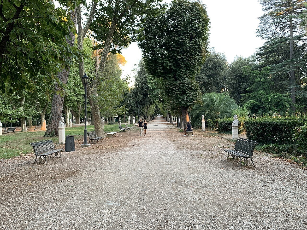 A gravel avenue lined with trees and benches in the Villa Borghese