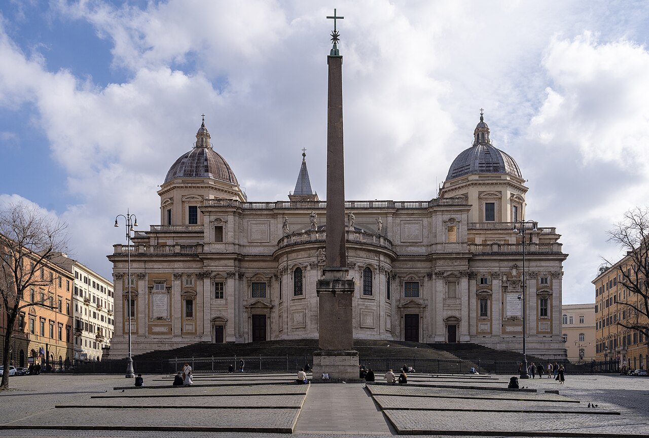 The apse of Santa Maria Maggiore behind its tall obelisk, two domes against a cloudy sky