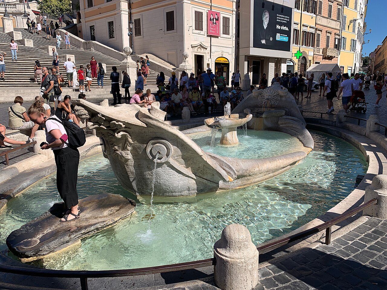 A visitor leaning over the Barcaccia fountain, the Spanish Steps crowded behind