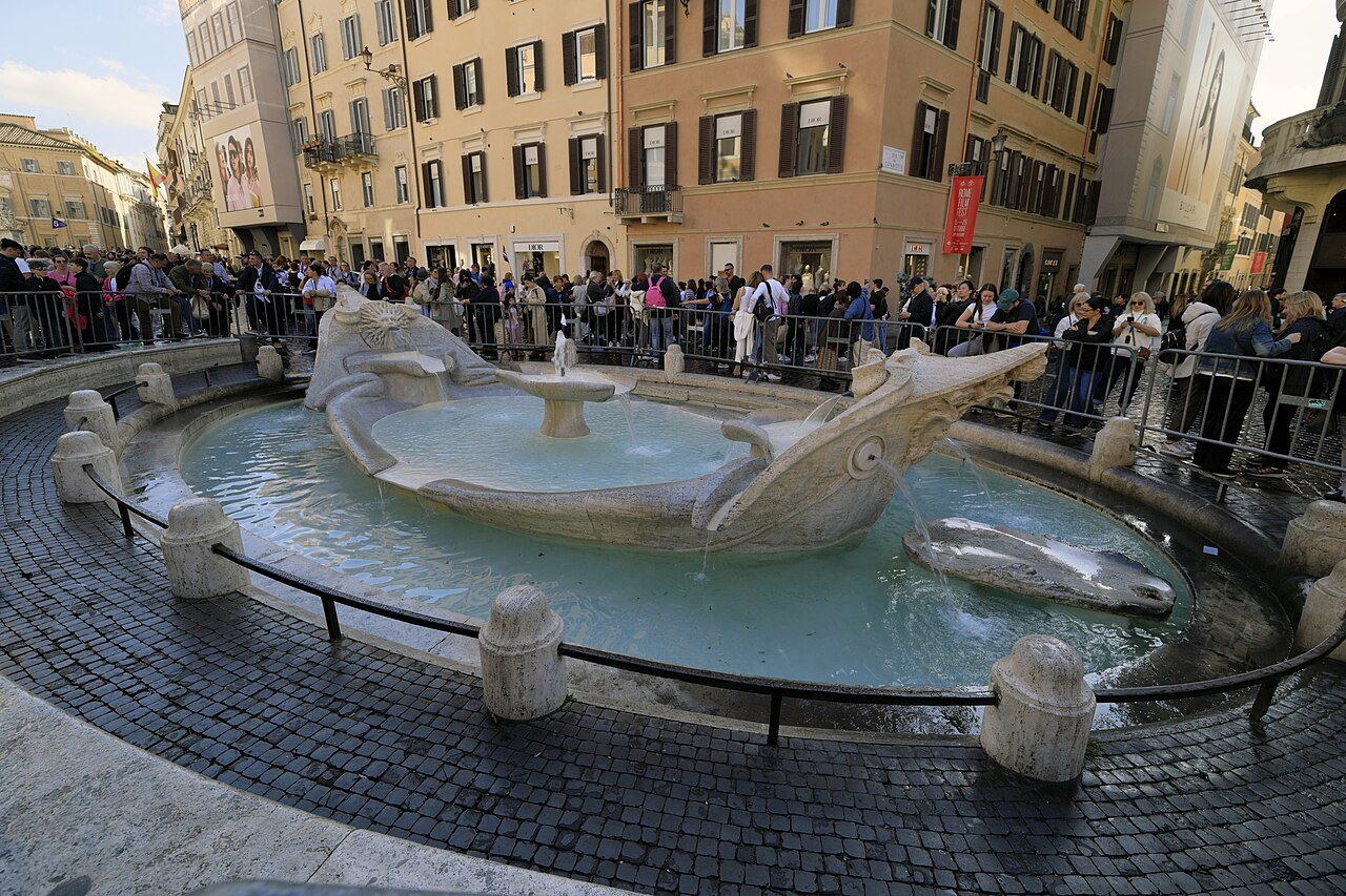 The Barcaccia fountain in Piazza di Spagna, a crowd along the barrier behind it