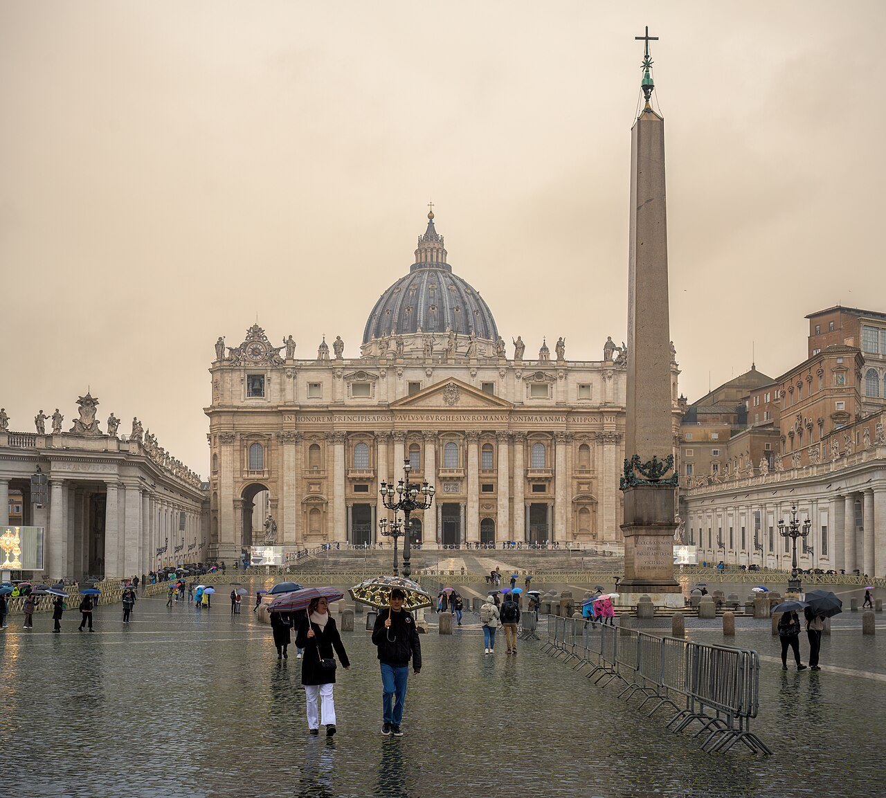 St. Peter's and its obelisk on a gray, rainy day, a few visitors crossing the square