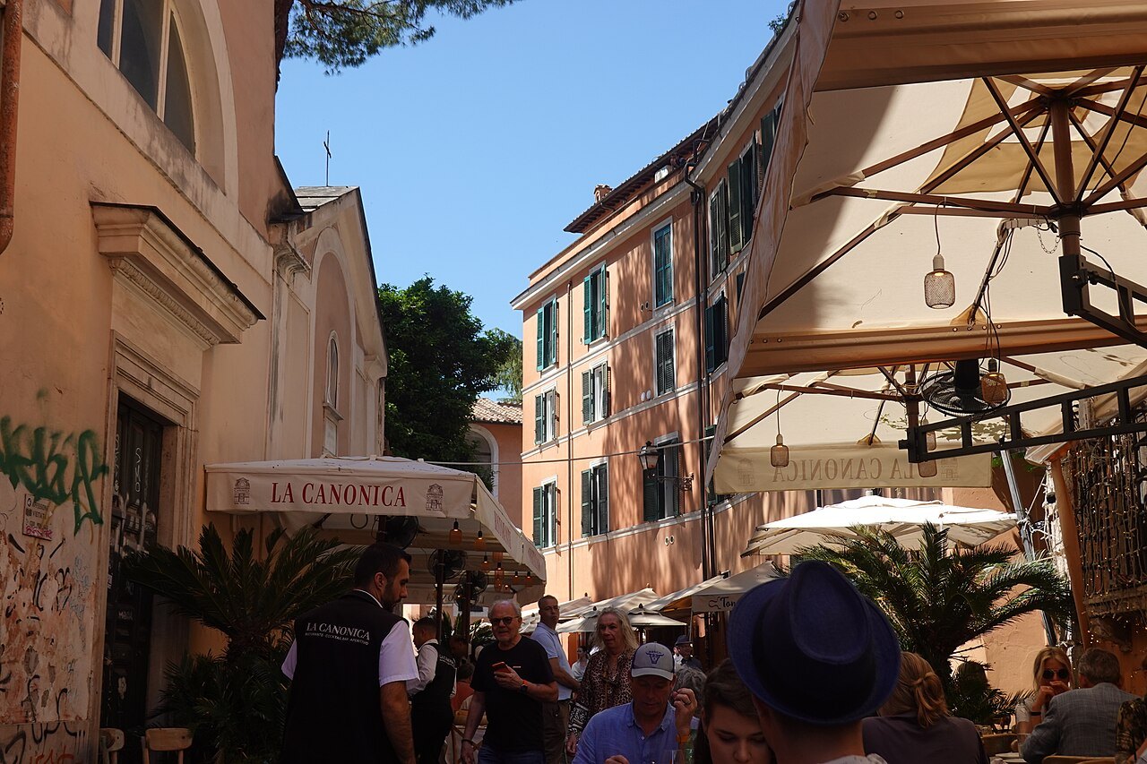 Vicolo del Piede in Trastevere, café awnings and a crowd in the narrow lane