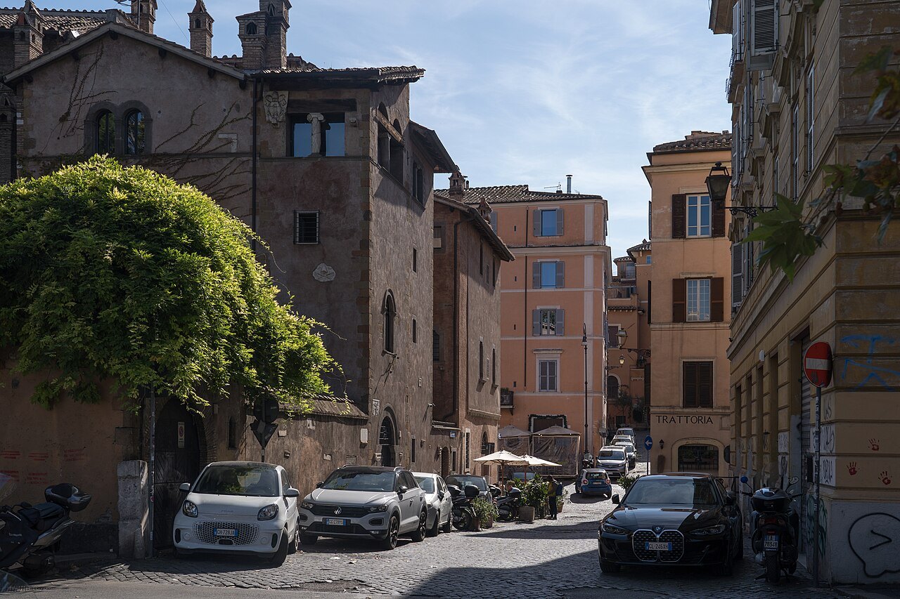 A small square in Trastevere with old brick and ocher houses, cars parked on the cobbles