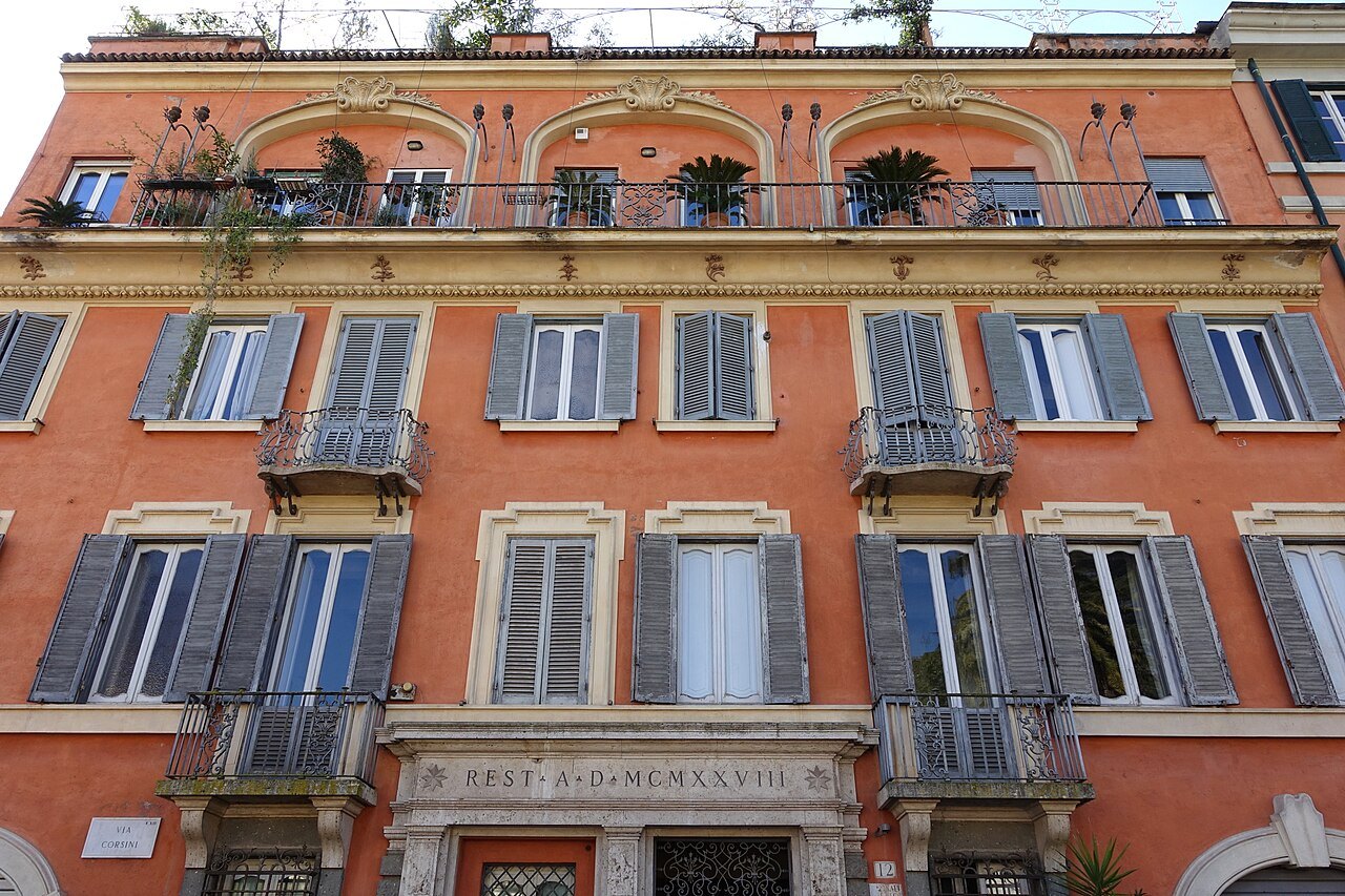 An orange palace front on Via Corsini with green shutters and an inscription over the door