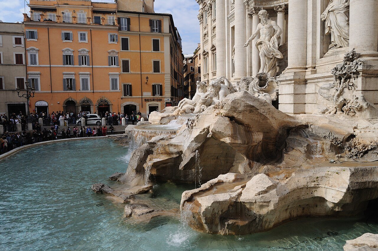 Water pouring over the carved rocks into the Trevi Fountain's basin, houses across the square