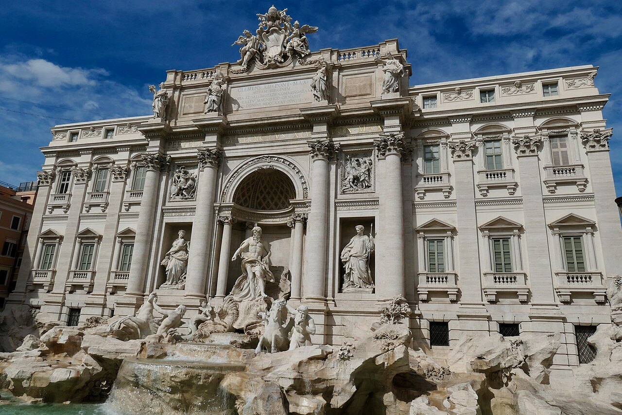 The Trevi Fountain against a deep blue sky, its rocks and statues in full light
