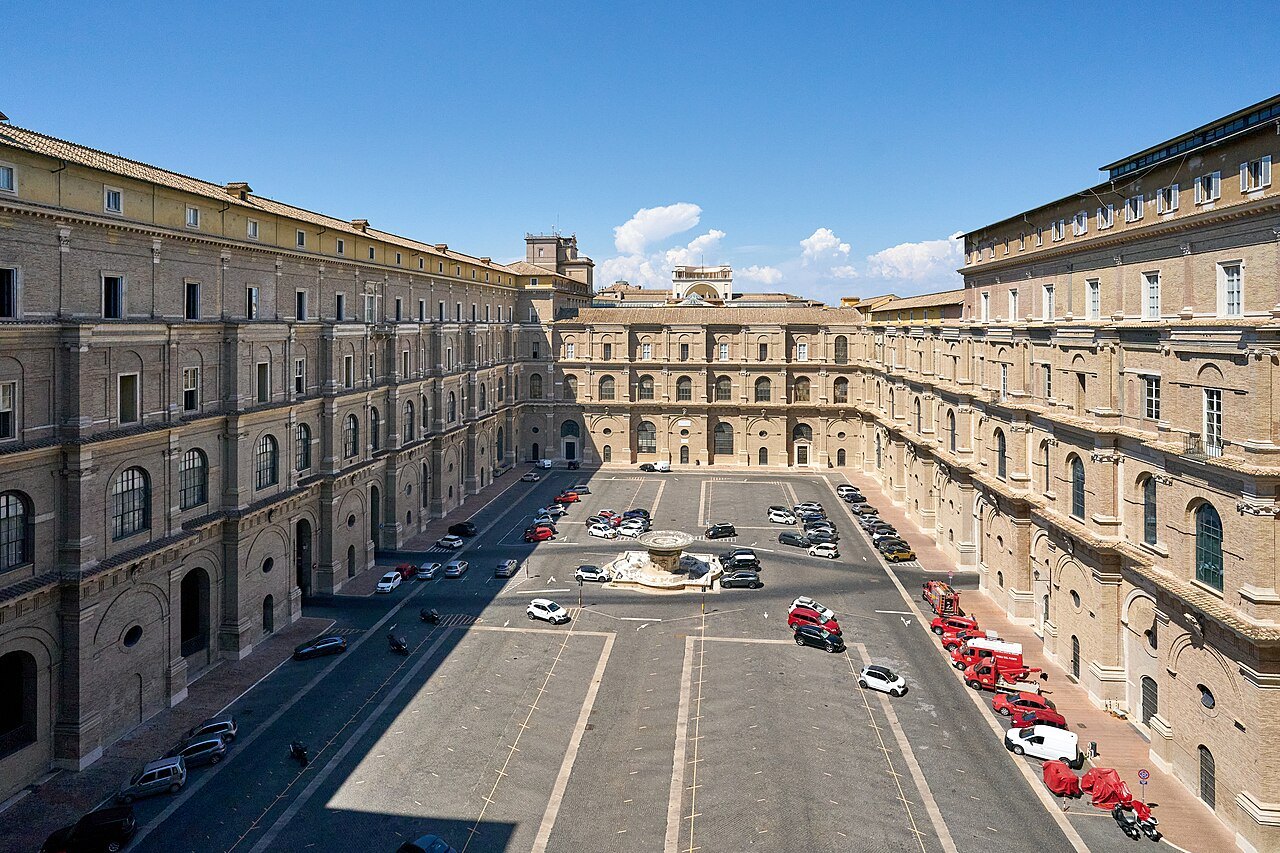 A long courtyard of the Vatican palaces seen from above, cars parked along it