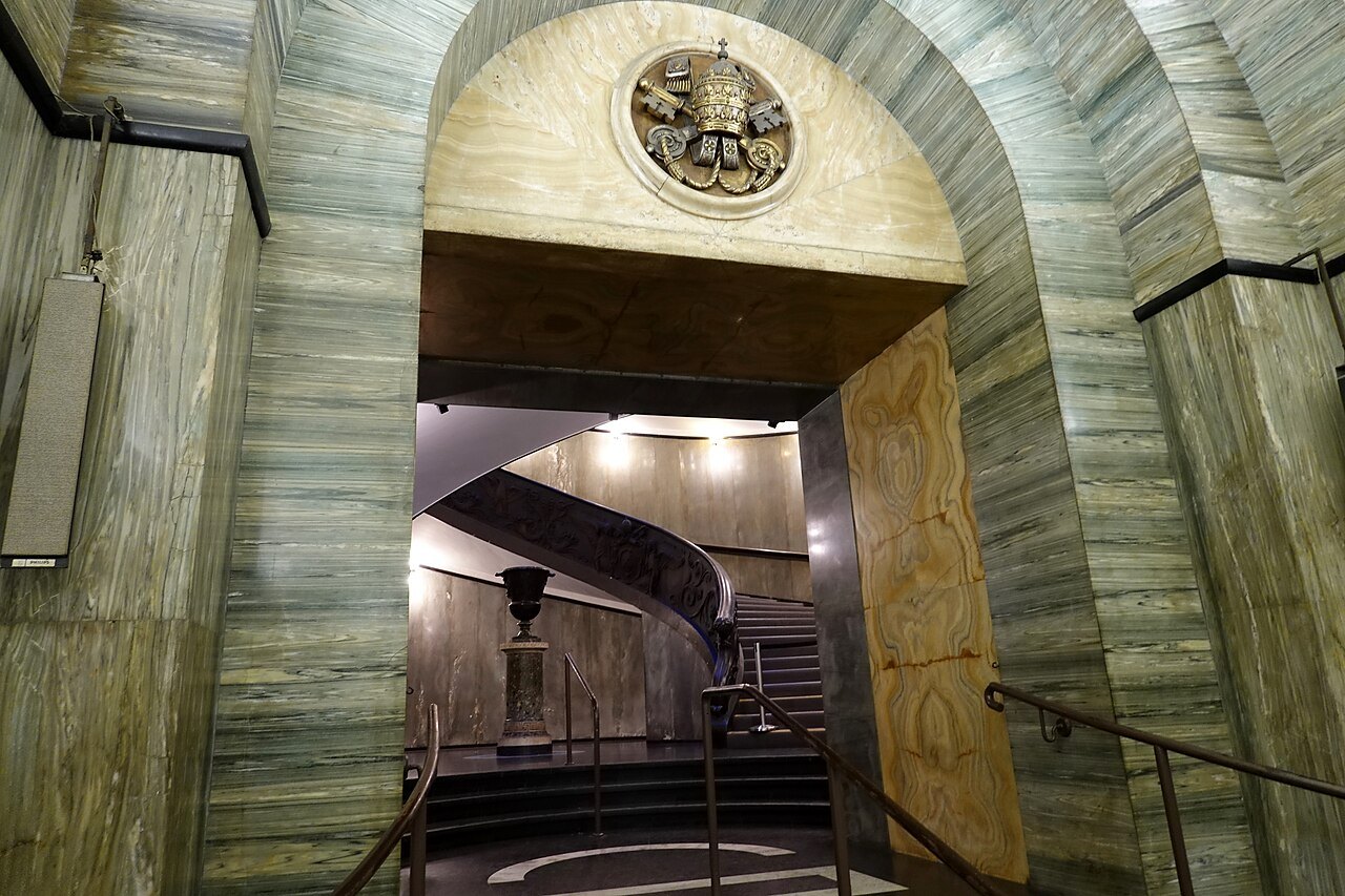 The entrance to the Vatican Museums, a stair spiraling down beyond the bronze doorway